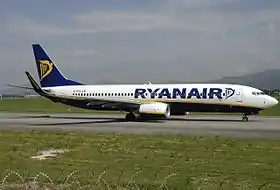 Avion blanc avec le bas-ventre noir, une harpe jaune sur la queue bleu marine de l'appareil. Il est sur une piste, le nez dirigé vers la droite de l'image.