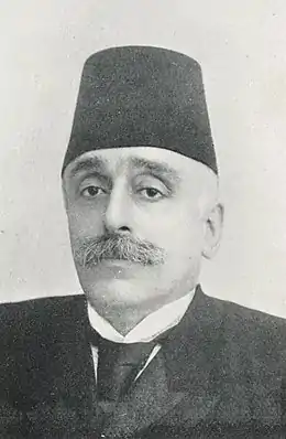 Portrait d'un homme moustachu portant un fez, un costume et une cravate.