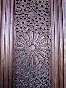 Gros plan sur le décor sculpté d'un panneau des dormants de la grande porte de la salle de prière. Ce décor est constitué d'une rosace, d'entrelacs géométriques et de fleurs.