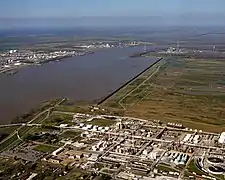 Photo aérienne d'un cour d'eau au bord duquel se trouvent une usine et un champ vide.