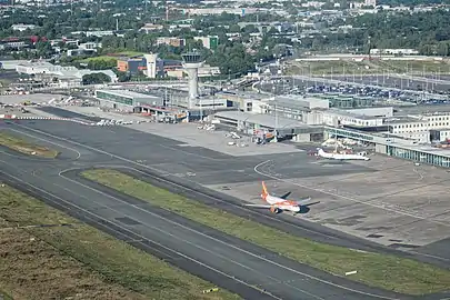 Photographie aérienne de l'aéroport. On y voit une piste de décollage et un bâtiment voyageur.