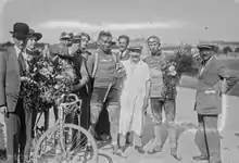 Photographie en noir et blanc montrant des cyclistes recevant des récompenses à l'arrivée d'une course.