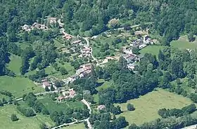 photo aérienne représentant un village entouré de bois et de champs.