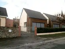 Photographie en couleurs d'un ensemble de bâtiments en bois et pierre ; inscription « école » au-dessus du porche.