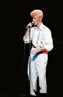 Photo d'un homme blond entièrement vêtu de blanc en train de chanter dans un micro
