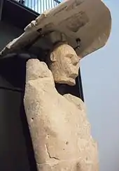 Une statue en pierre blanc crème humanoïde avec un bouclier comme un chapeau au-dessus de la tête.