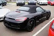 Photo d'une Boxster GTS vu de 3/4 arrière sur un parking, avec une capote et des jantes Carrera S noires.