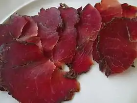 Photo couleur d'une assiette de très fines tranches de viande rouge cramoisi à grain fin légèrement marbrée de rose clair et bordé d'une teinte plus sombre brune violacée.