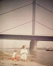 Photographie couleur ancienne d'un pont à haubans vu de la rive.