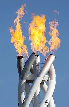 Photographie d'une torche en flamme, à trois bras entrelacés.
