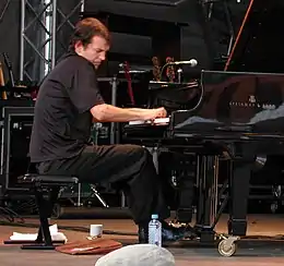 un homme sur scène, habillé en noir, en train de jouer du piano