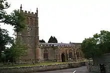 Photo d'un bâtiment à un étage avec des fenêtres en ogive, flanqué d'une grande tour carrée à gauche avec une horloge