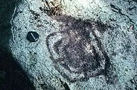 vue d'un dessin gravé en noir sur la surface blanche et rugueuse d'une pierre.