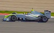 Vue de gauche d'une monoplace de Formule 1 blanche, aux liserés jaune fluo et noir, en piste