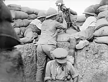 Trois soldats entourent une mitrailleuse disposée au sommet d'une tranchée surélevée avec des sacs de sable.