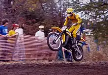 Motard habillé de jaune sur une moto jaune, en plein saut durant une course de moto-cross.