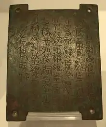 Photographie d'une petite plaque de bronze gravée de sinogrammes anciens.