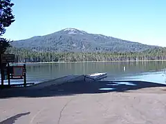  Un parking, un lac bordé d'une forêt derrière, et une montagne qui est légèrement inclinée dans l'arrière-plan.