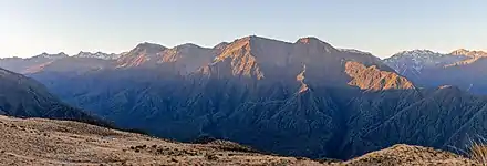 Chaine de montagnes brunes au sol peuplé d'herbes rases, et mises en relief par un éclairage rasant.