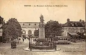 Carte postale ancienne montrant une motrice du tramway de Troyes derrière le monument des Enfants de l'Aube, et, en arrière-plan, la gare.