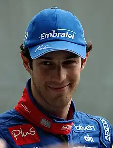 Photo en portrait d'un homme blanc, brun, de face, en tenue de pilote bleue, avec une casquette bleue, souriant.