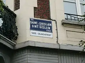 Photographie d'une plaque de rue sur fond bleu et blanc, apposée sur un mur.