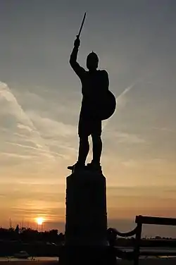 Photo montrant la statue d'un homme brandissant une épée se découpant en silhouette devant le soleil couchant.