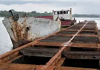 Photographie couleur d'un bateau rouillé amarré le long d'un ponton endommagé.