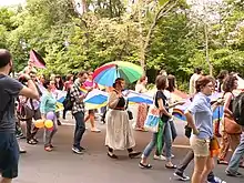 Photographie de la marche des fiertés 2014 à Bucarest. Une partie du cortège de manifestants et manifestantes, portant un immense drapeau arc-en-ciel.