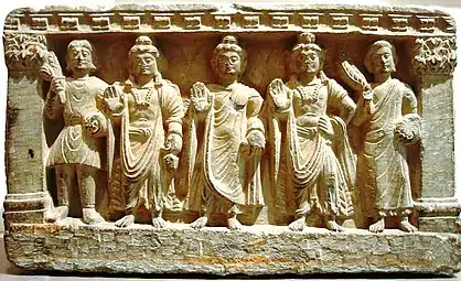 Une triade précoce du bouddhisme mahāyāna. De g. à d. un dévot kouchan, le Bodhisattva Maitreya, le Bouddha, le Bodhisattva Avalokiteshvara, et un moine bouddhiste. IIe-IIIe siècle, Gandhara.