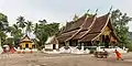 Jeune moine bouddhiste poussant un chariot pour rejoindre d'autres occupés à nettoyer la cour du temple Vat Xieng Thong. Juin 2018.