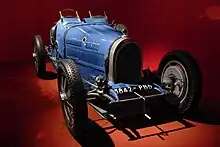 Photographie d'une automobile des années 1920, de couleur bleu azur, vue de trois-quarts, en exposition dans un musée.