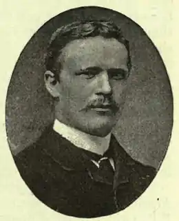Photographie en noir et blanc en médaillon d'un homme aux cheveux courts et à la courte moustache.