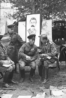 Photographie en noir et blanc de militaires nazis et soviétiques discutant devant un portrait de Joseph Staline.