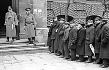 Grande file d'attente de Juifs pour l'enregistrement au travail forcé du ghetto, devant l'ancienne école de commerce, à l'intersection de la rue Prosta avec Waliców, qui abrite alors différentes institutions gouvernementales (mai 1941)