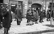 Passants à côté d'un enfant juif en haillons allongé sur le trottoir, endormi, malade ou mourant, rue Leszno (mai 1941)