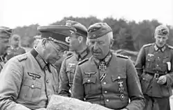 Photographie en noir et blanc d'un groupe d'hommes, portant des uniformes, consultant une carte.