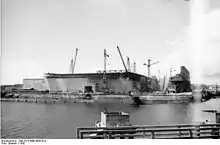 Plan large présentant un chantier de construction au bord du bassin du port de Lorient. De nombreuses grues sont visibles au-dessus d'une structure massive en béton armé.