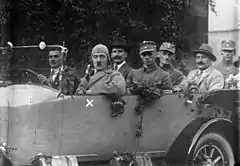 Photographie en noir et blanc de Adolf Hitler en tournée de propagande en 1923. Il est assis à bord d'une voiture, au premier plan à gauche de l'image