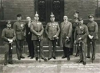Photographie en noir et blanc des principaux accusés du procès. Ludendorf, en uniforme et arborant ses décorations est au centre de l'image, Hitler est immédiatement à sa gauche
