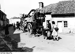 Photo en noir et blanc de gens chargés de bagages passant à pied ou en charrette entre des maisons basses