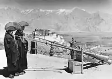 Photographie en noir et blanc de deux moines tibétains soufflant dans des trompes