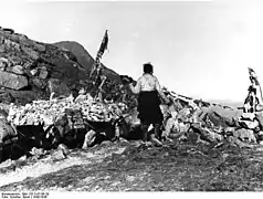 Photographie en noir et blanc d'un homme en habits traditionnels tibétains de dos passant le col.