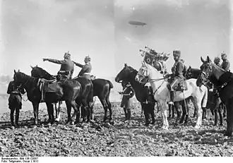 Photo de la suite impériale à cheval, avec les trompettes des garde du corps en train de sonner, le tout surmonté par un dirigeable.