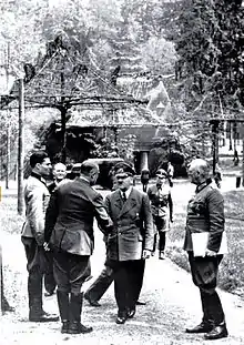 Photographie en noir et blanc montrant Claus von Stauffenberg, à gauche en veste claire, Adolf Hitler et Wilhelm Keitel à droite