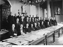 Photo de groupe d'officiers posant en tenue civile devant des documents d'archives