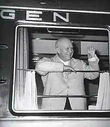 Photographie d'un homme souriant saluant depuis la fenètre d'un wagon