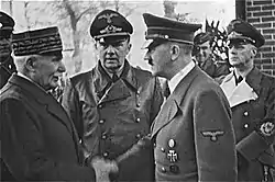 Le maréchal en képi serre la main d'Hitler en uniforme avec casquette, encadrés de deux Allemands en uniforme.