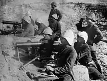 Photographie de deux mitrailleuses disposées derrière un talus et manœuvrées chacune par quatre hommes