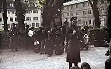 Deux personnes armées en uniforme gardent un groupe d'une quinzaine de personnes composé surtout d'enfants.